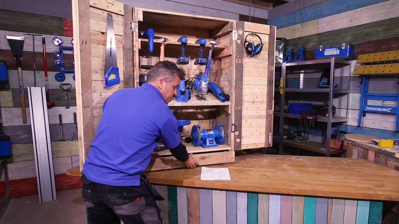 Man opening the drawer of a storage cabinet made from wood pallets