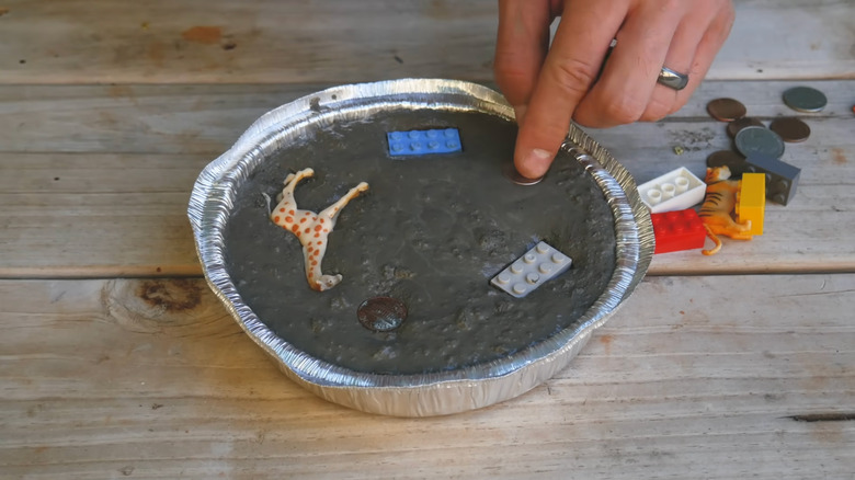 A person pushes assorted items into a disposable tin filled with concrete