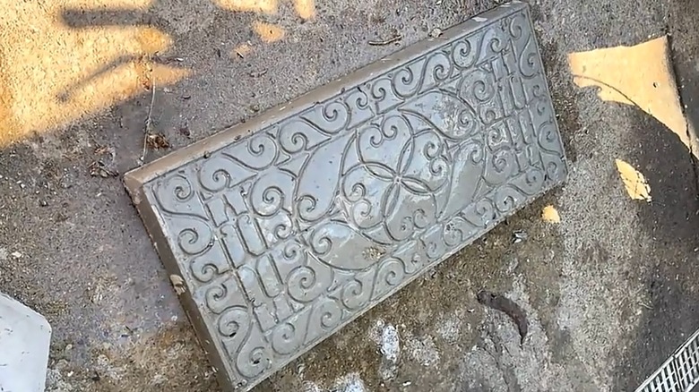 The scrollwork design from a decorative boot tray is pressed into a DIY concrete paver