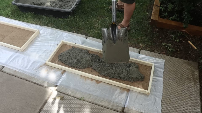 A man shovels concrete into a wood paver form