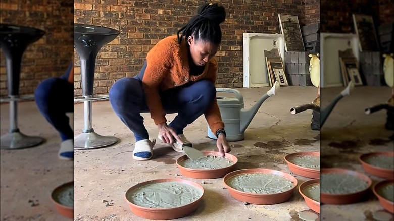 A woman crouches on the ground while smoothing concrete inside plant saucers