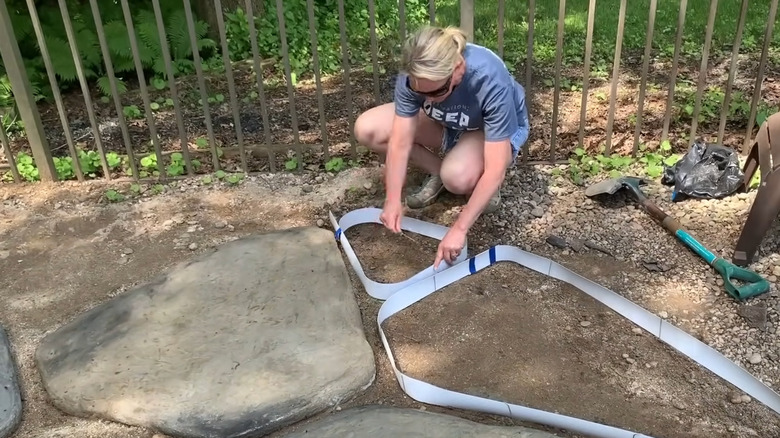 A woman crouches to arrange vertical vinyl blinds into a stone paver shape