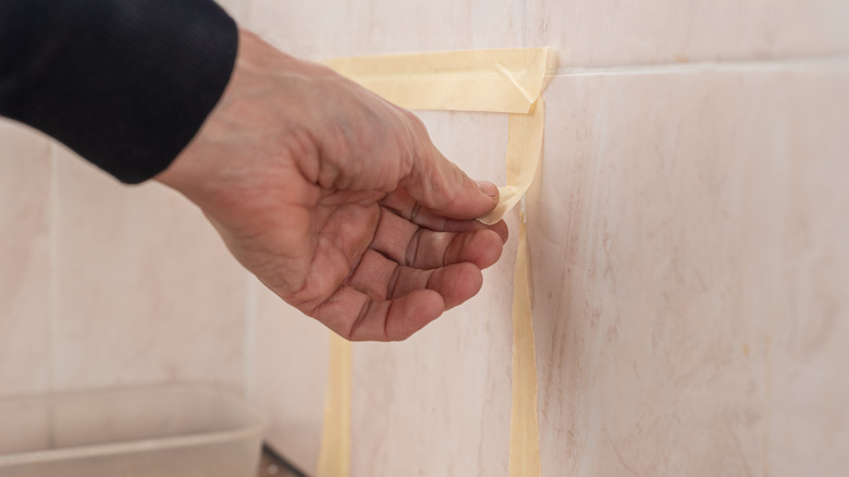 a hand is shown removing masking tape from a tile wall