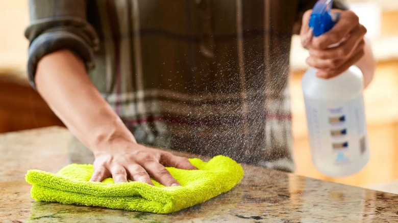 a woman sprays cleaner on a countertop and wipes it with a neon yellow microfiber cloth