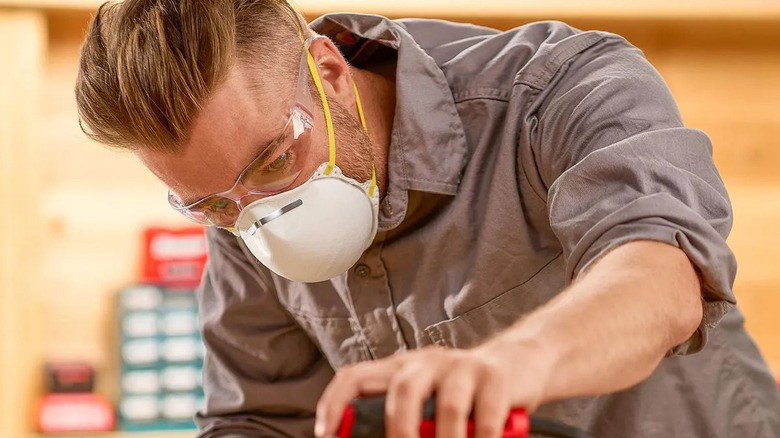 a man wears a white respirator mask while using a power tool