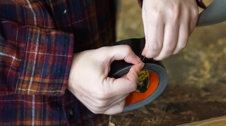 A person wearing a plaid flannel shirt rips a piece of Gorilla duct tape