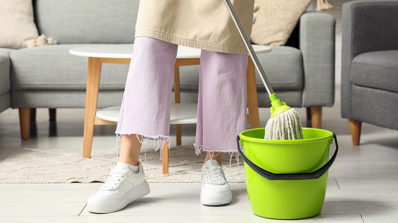 A woman wearing lavender pants mops a floor