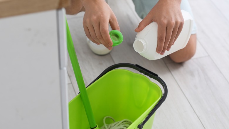 Hands pouring a bottled liquid into a mop bucket