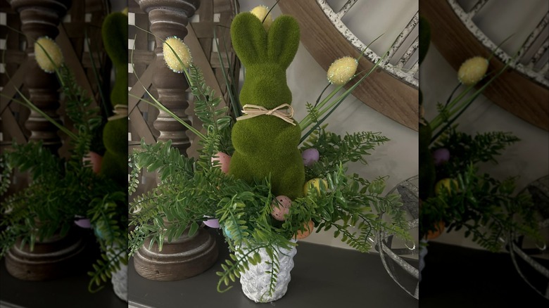 A flocked green bunny figurine sits in a pot of flowers on a table as part of a spring vignette.