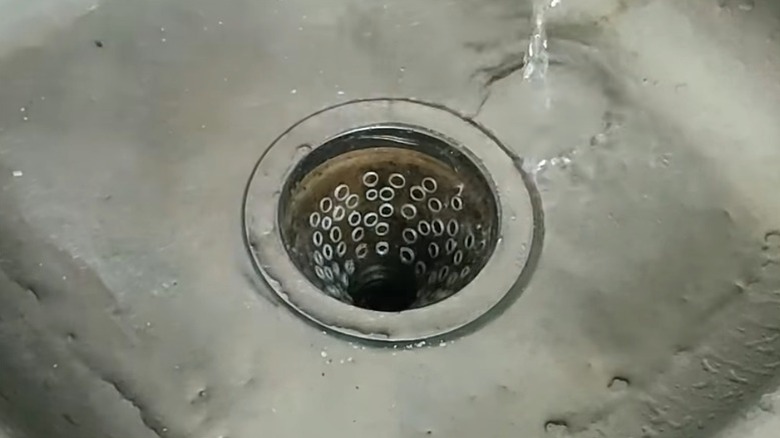 DIY basket strainer made from plastic water bottle in sink with tap running