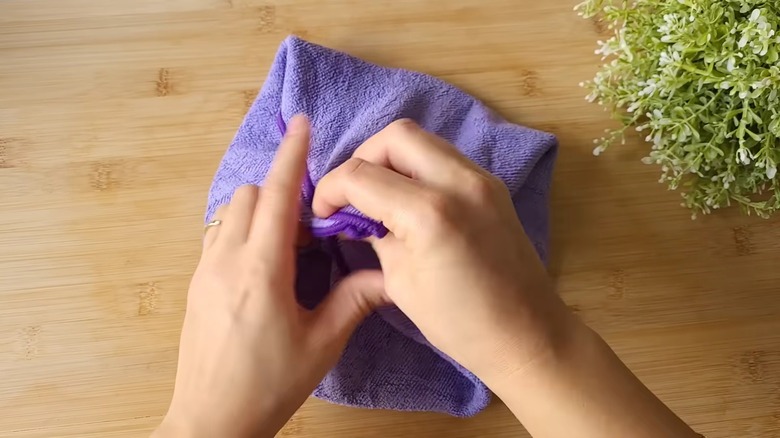 A hand holding a pot lid wrapped in a towel ready to clean a couch.