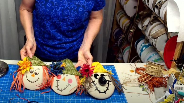 A woman holding up three scarecrow decor pieces made from pot lids.