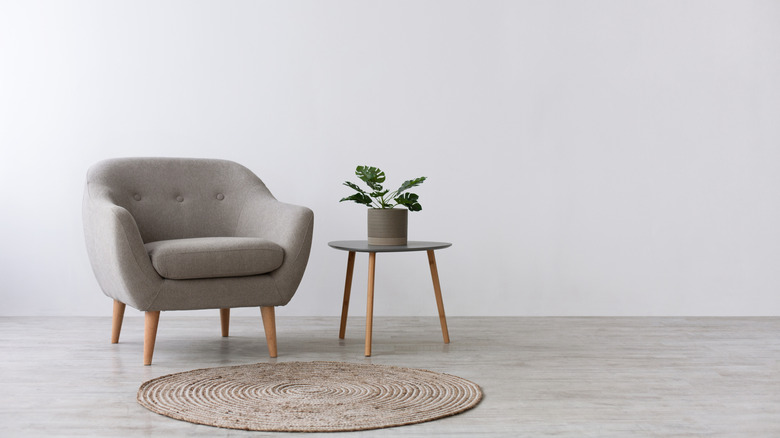 a room with a chair, rug, side table and plant, boring flat walls
