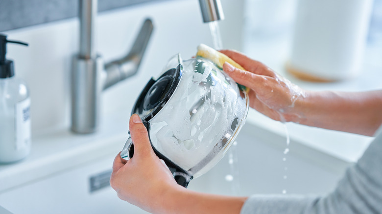 a woman cleans a coffee pot with a sponge