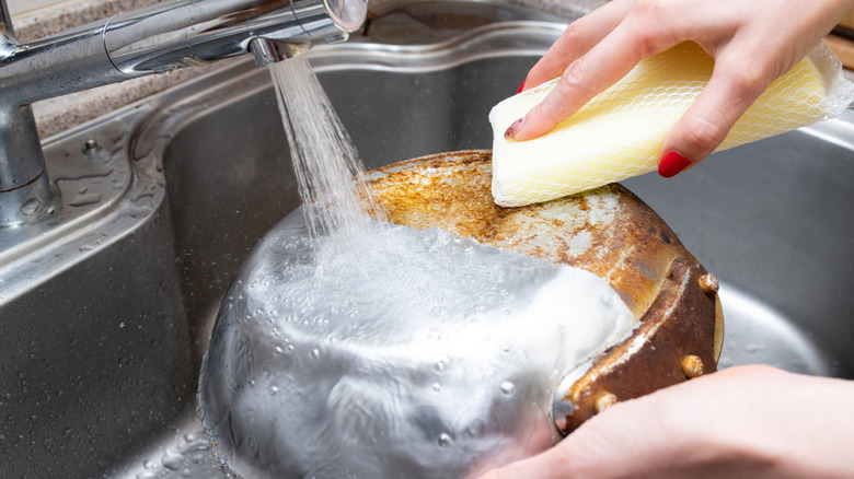 a woman cleans a pot with a sponge
