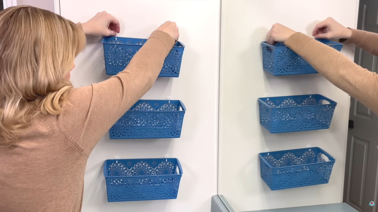Blonde woman hanging blue organizer bins on bathroom wall