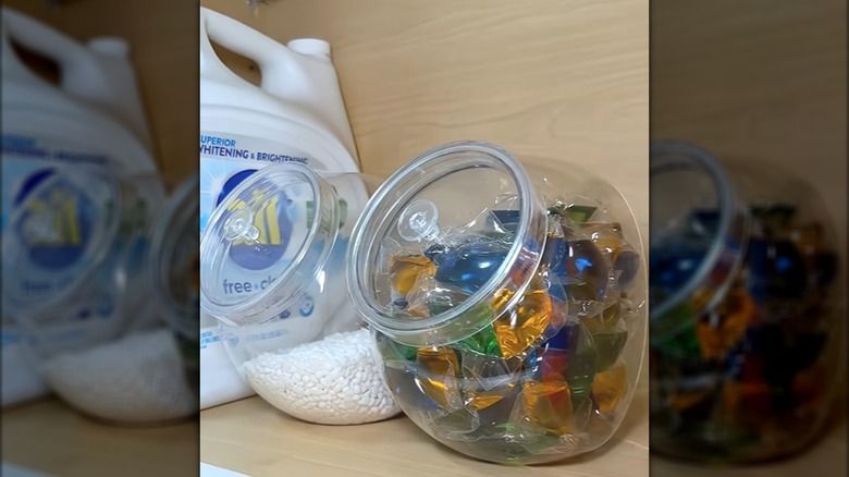 Laundry supplies tucked into glass cookie jars on wood shelf in laundry room