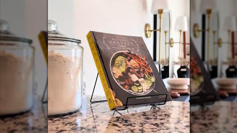 Cookbook on metal stand on granite counter beside jar