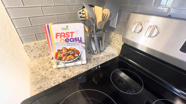 Small cookbook in metal napkin holder beside cooking utensils and stove