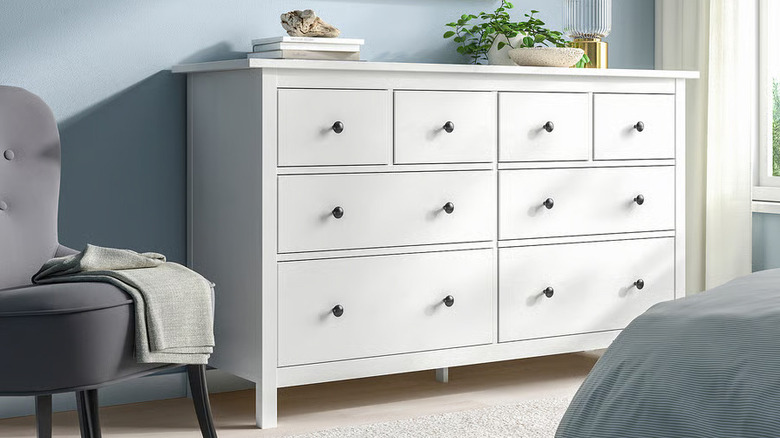 A stack of books and low potted plant sit on a white HEMNES dresser from IKEA