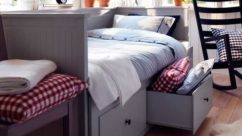 The drawer of a gray HEMNES daybed from IKEA is opened to hold colorful pillows