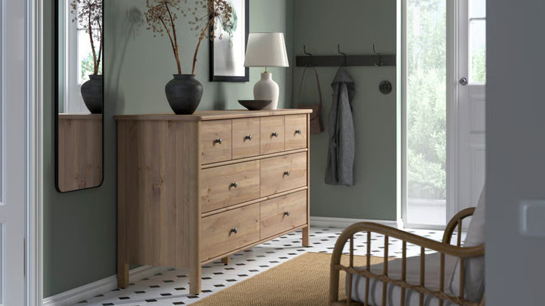A light brown wood STOREMOLLA dresser from IKEA displays decorative items in a sage green entryway
