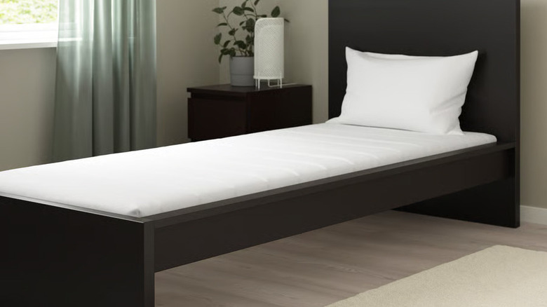 A white twin ÅSVANG Foam mattress from IKEA sits inside a modern black bed frame