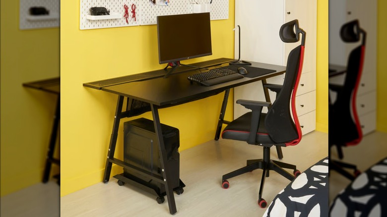 A black and red chair sits in front of a gaming desk in a bright yellow room
