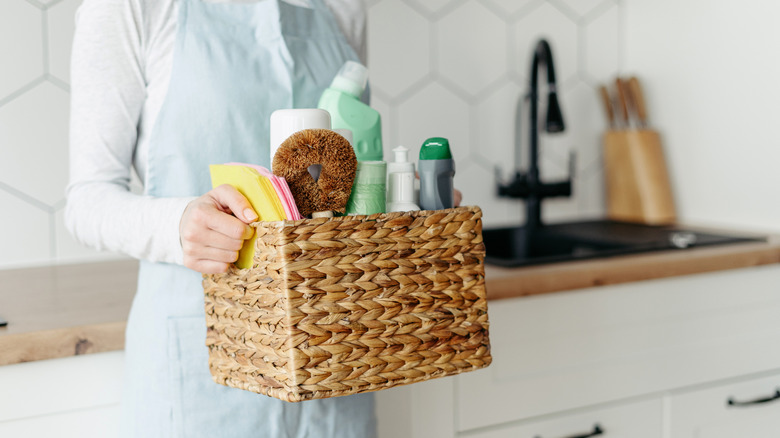 woman holding a woven basket full of cleaning supplies