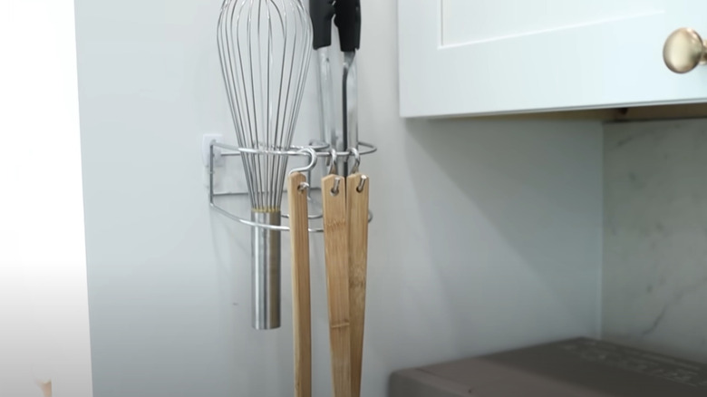 A napkin holder mounted to the wall to hold kitchen utensils.