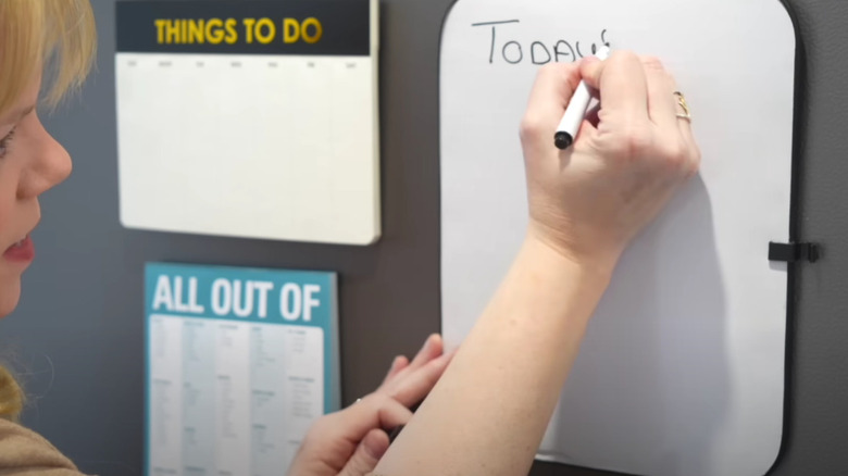 A woman writing a message on a white board magnetized to a fridge.