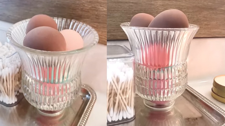Makeup sponges sitting in a flared glass vase on a silver bathroom tray