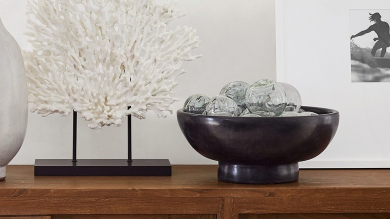 Black stoneware bowl filled with glass orbs beside expensive nautical coral decor