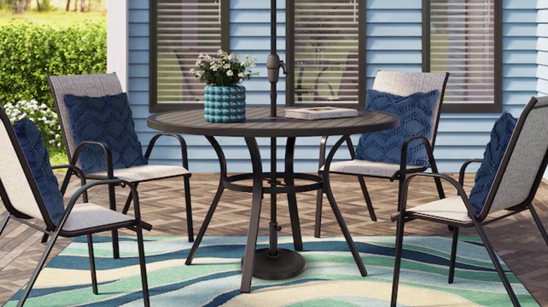 Four black and tan outdoor chairs with blue pillows sit around a large patio table