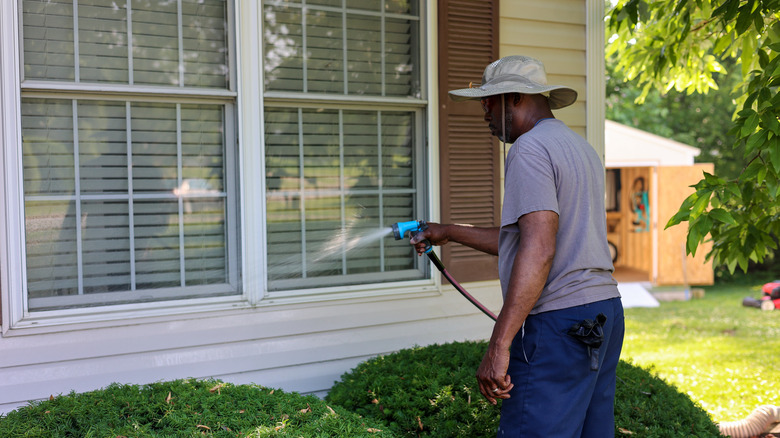 A man using a hose to wash outdoor windows on his home