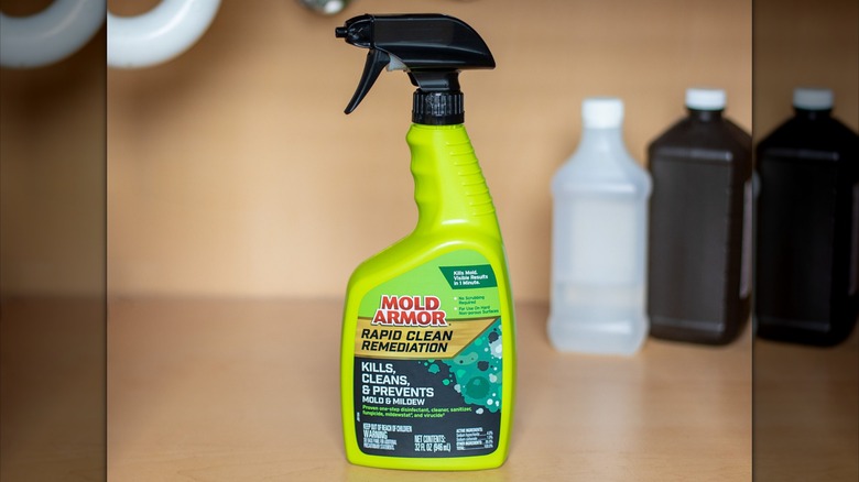A neon green bottle of Mold Armor Rapid Clean Remediation sits in a wooden cupboard