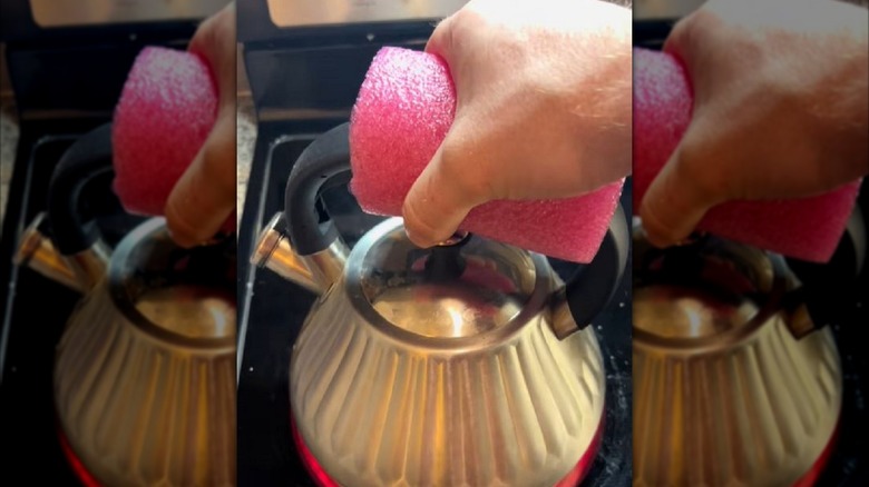 Hand grabbing tea kettle handle with pool noodle.