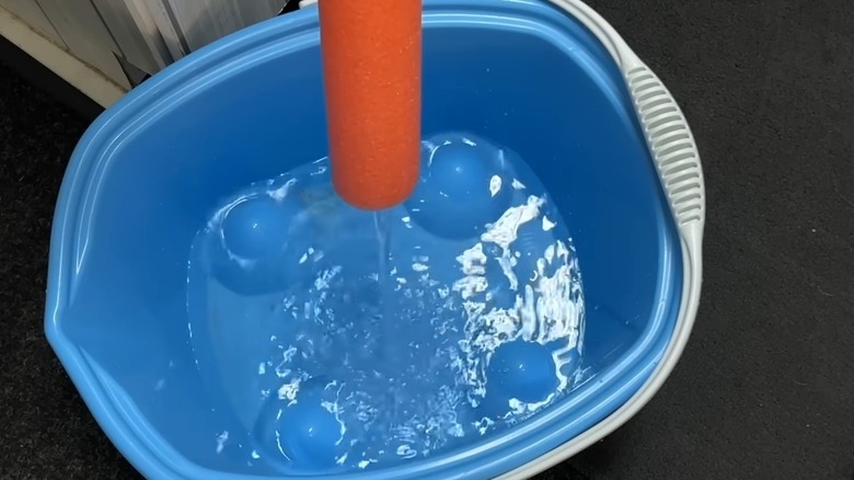 Person filling large bucket using pool noodle.