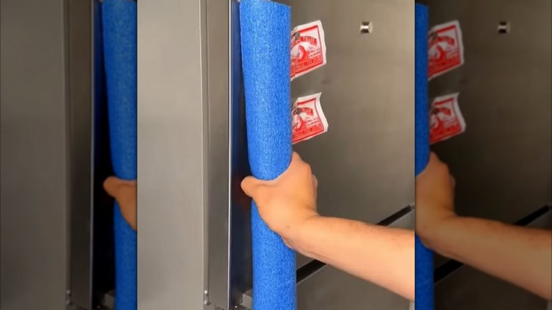 Hand holding refrigerator door handle covered by pool noodle.