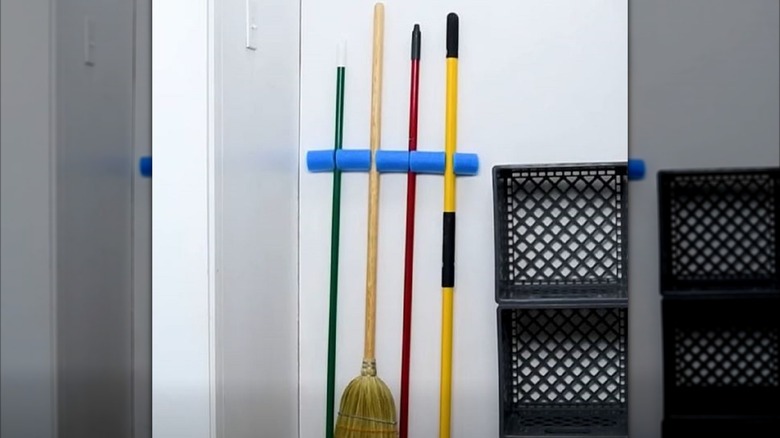 Brooms and mops mounted on wall in pool noodle holder.