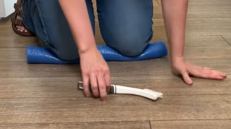 Woman using pool noodle to protect knees while cleaning kitchen floor.