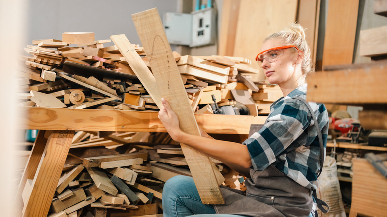 woman wearing glasses and holding two wood boards picked from a pile of scrap wood beside her
