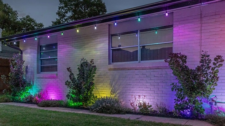 Outdoor landscaping lights cast a colorful glow on the side of a brick ranch