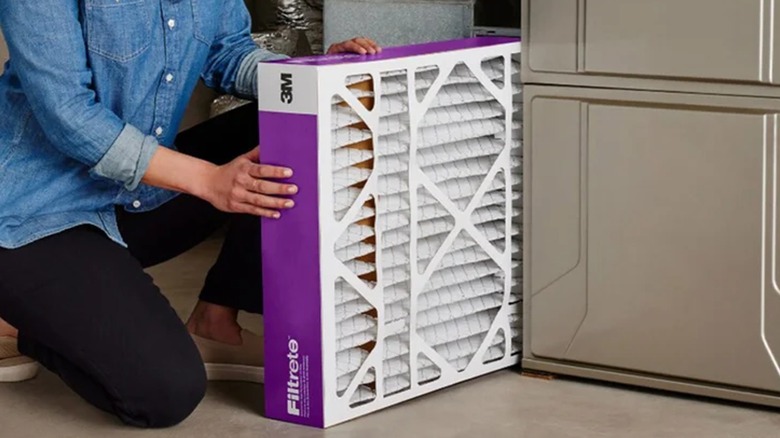 A person kneels while holding a new air filter