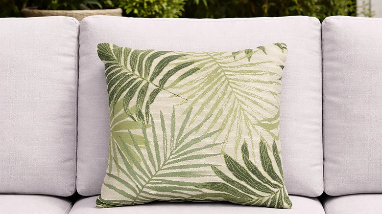 A green palm-covered throw pillow sits on a gray outdoor sofa