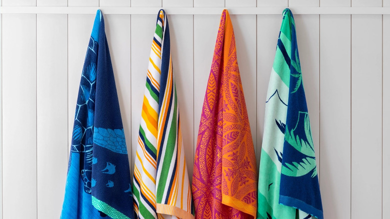 Four colorful beach towels hang on a white shiplap-covered wall
