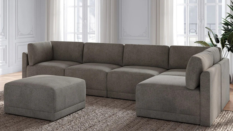 A dark gray sectional and matching ottoman sit in front of two large windows