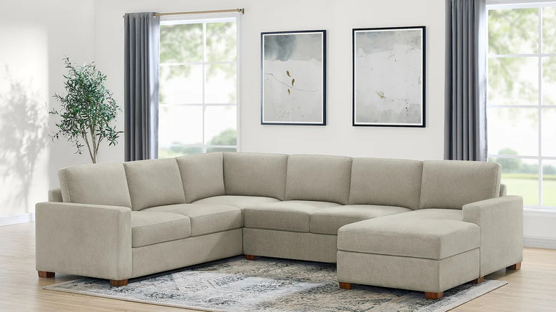 Two large prints hang over a beige sectional sofa