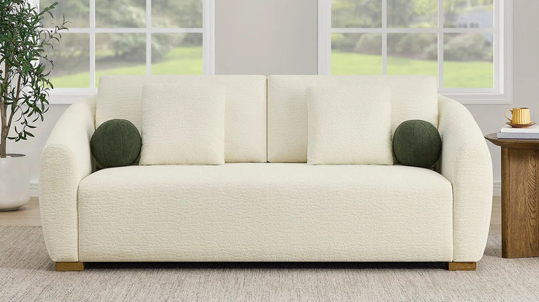 A potted tree and wooden side table flank a cream colored sofa