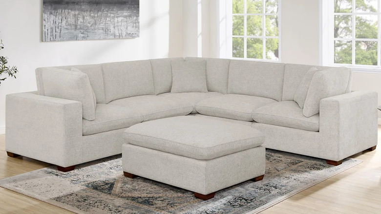 A light grey ottoman sits in front of a large matching sectional sofa